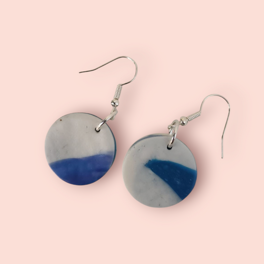 A pair of circular earrings with one side in gray and the other side in blue, attached to fish hook closures.