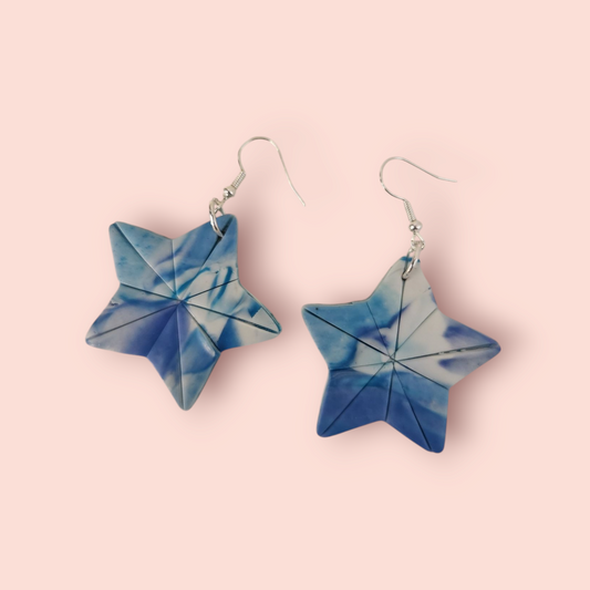 A pair of blue and white star-shaped earrings on a light background.