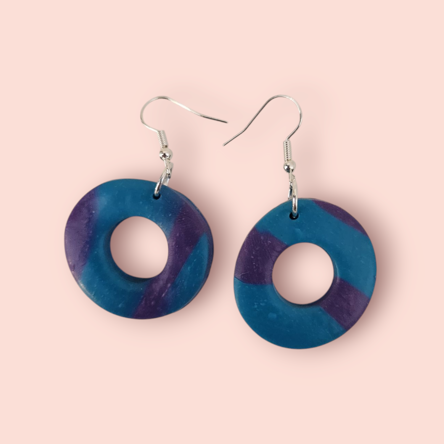 A pair of round earrings with a pattern of blue and purple stripes.