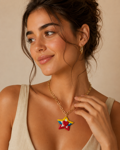 A woman wearing a gold chain necklace with a colorful star-shaped pendant featuring red, yellow, and blue segments, posed against a warm beige background.