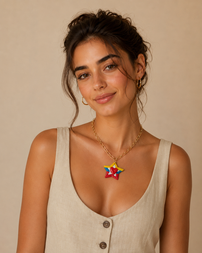 A woman wearing a gold chain necklace with a colorful star-shaped pendant, paired with a beige linen tank top, set against a solid beige background.