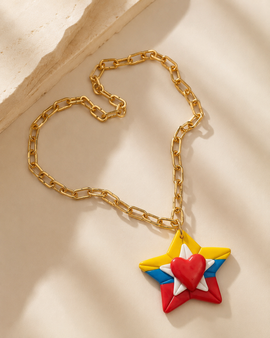 A gold chain necklace with a star-shaped pendant featuring the colors of the Philippine flag (yellow, blue, red) surrounding a small red heart, displayed on a warm beige surface with soft shadows.